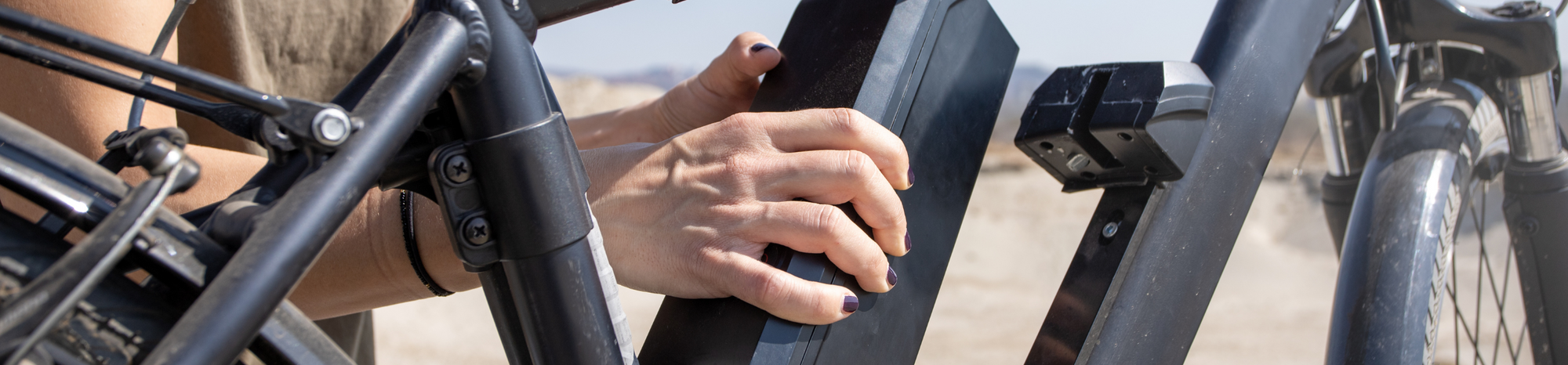 A hand securing a black rectangular e-bike battery onto a bicycle frame.